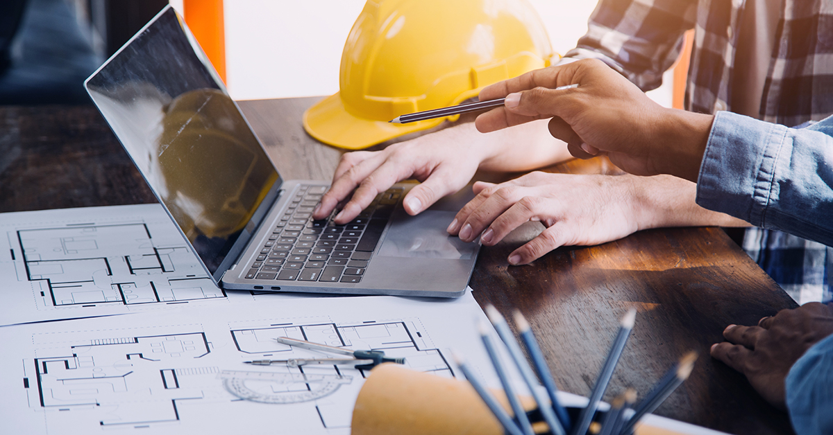 Two people pointing at a laptop and building blueprints