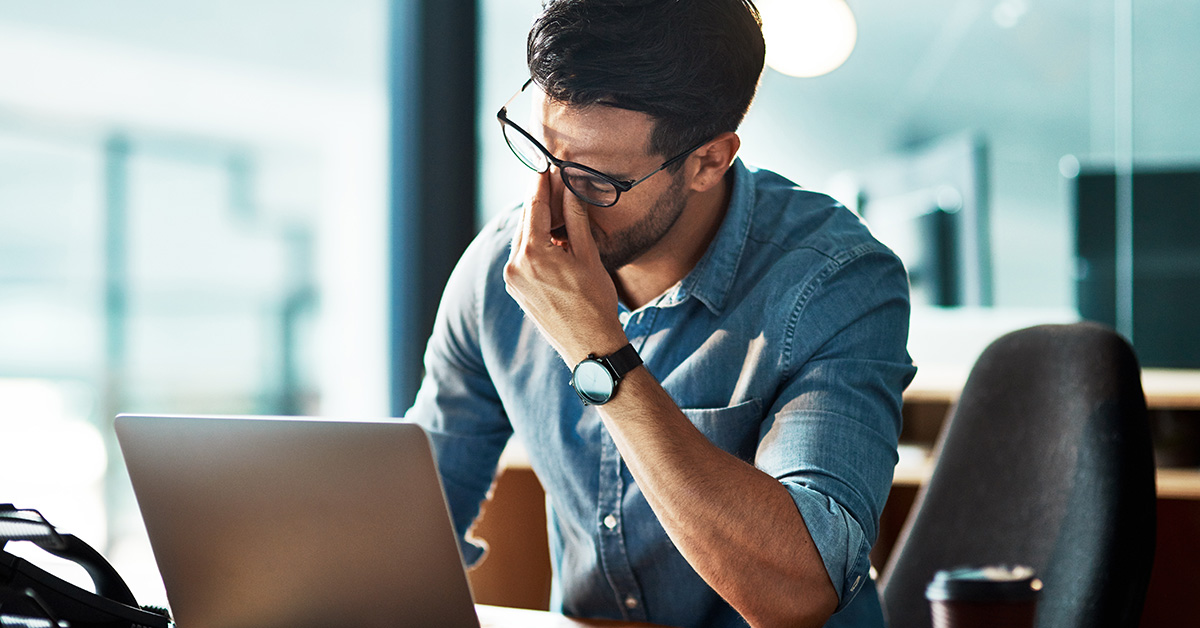 A man pinching the bridge of his nose in frustration in his office