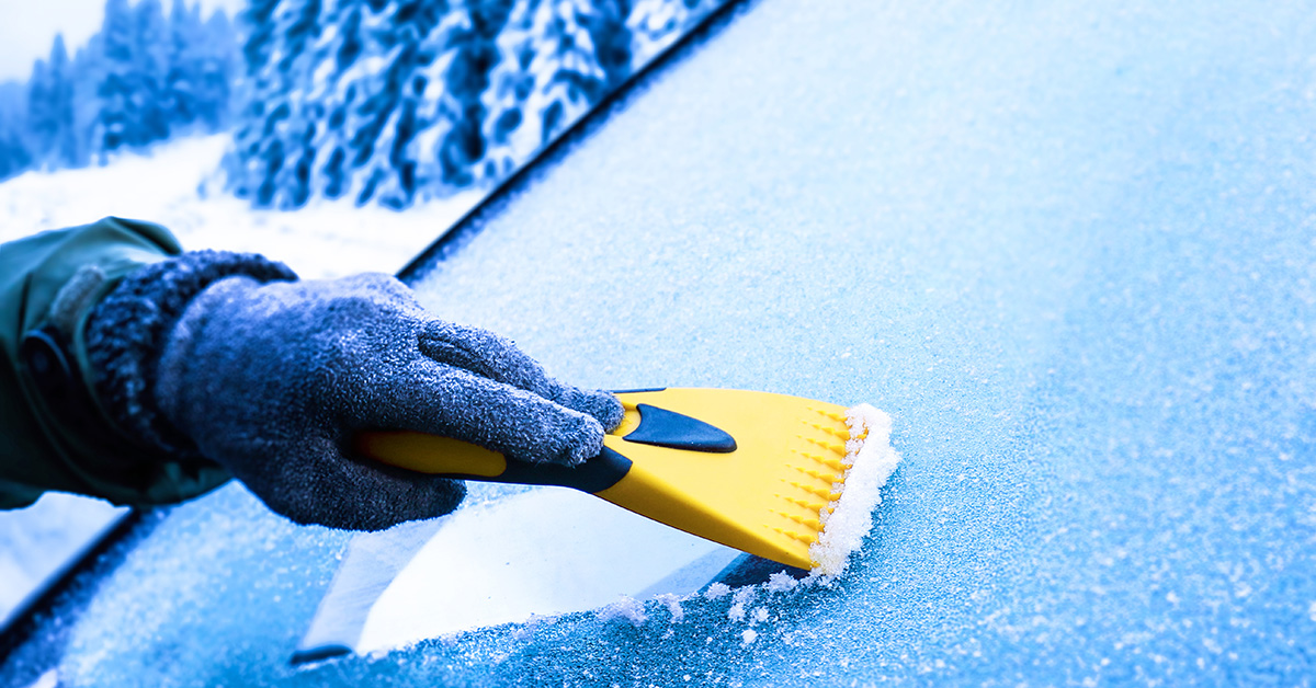 gloved hand removing ice from windshield with scraper