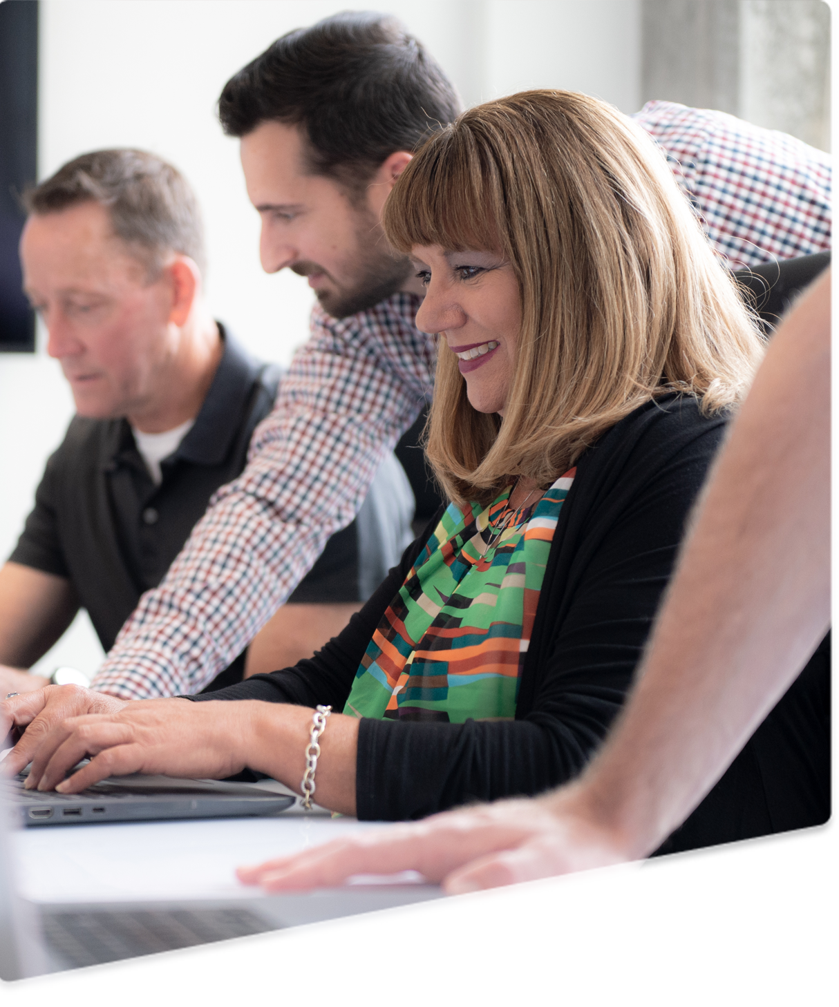three smiling people sitting at a table looking at information on a computer screen