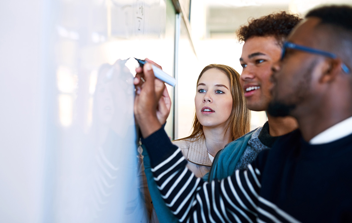 three students work together on a whiteboard
