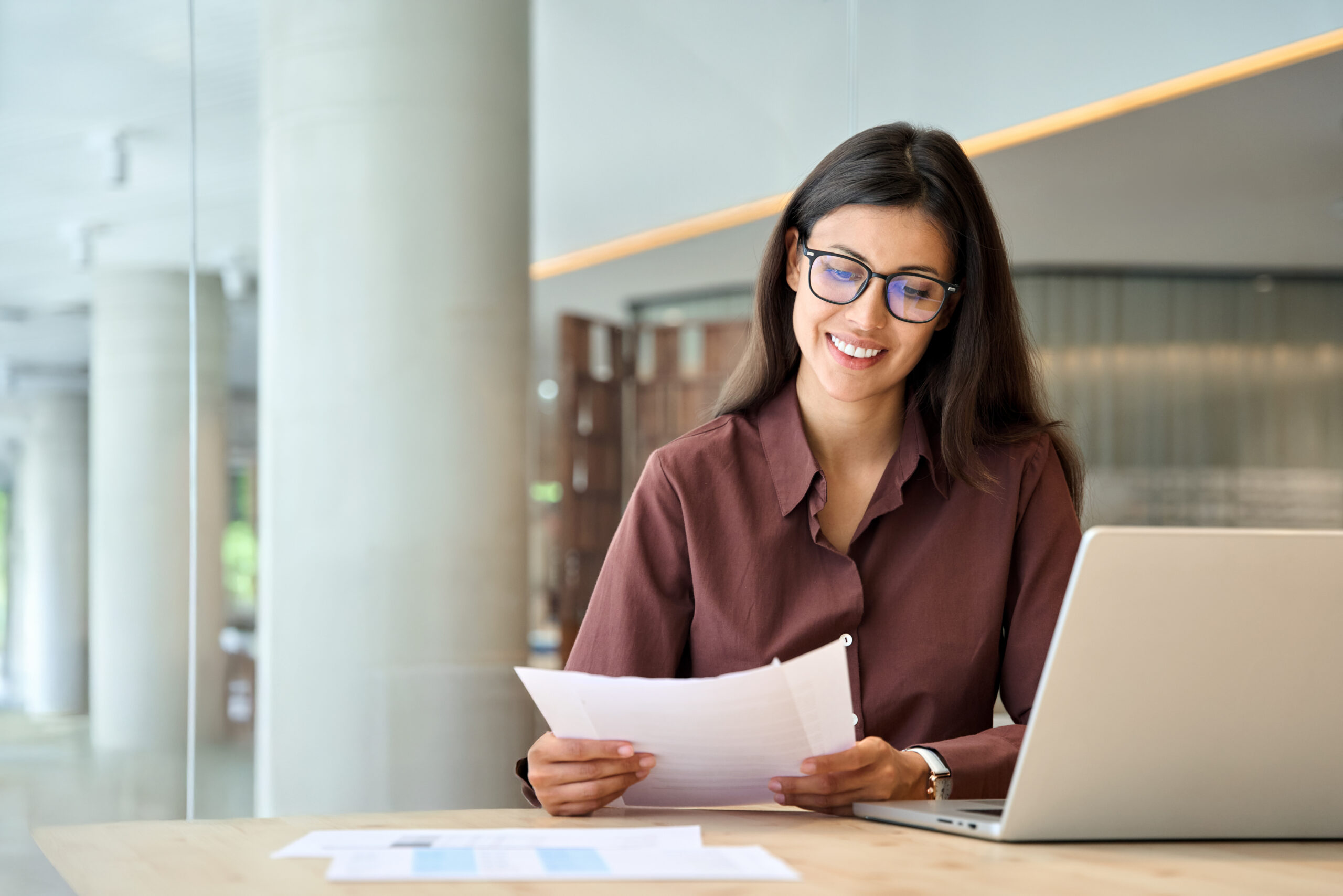 Smiling businesswoman doing paperwork using laptop